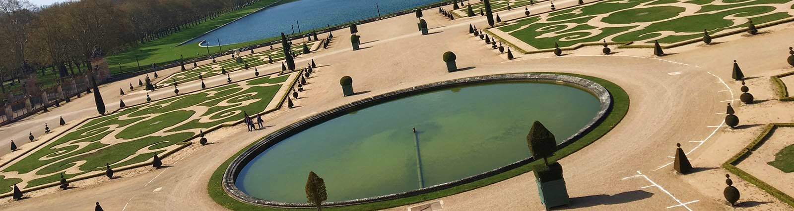 Paris Arc de Triomphe Skip the Line Rooftop Tickets Aerial view of formal French palace gardens with geometric hedges, manicured lawns, ornamental pond, and cypress trees lining